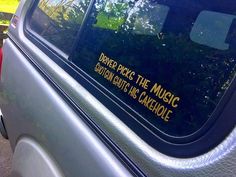 the back window of a silver car with yellow lettering on it and trees in the background