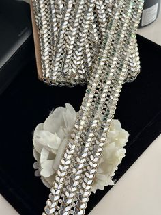 a pair of silver sequins and flowers on a black tray next to a cell phone