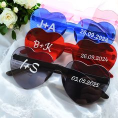 two heart shaped sunglasses with the names of each couple on them, sitting next to some flowers