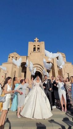 a bride and groom walking down the steps with their wedding party throwing white doves in the air