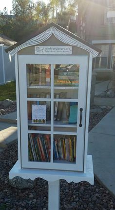 a white book case sitting on top of a gravel covered ground next to a sidewalk