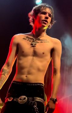 a shirtless man with tattoos on his chest standing in front of a red light