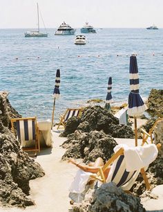 chairs and umbrellas on the beach with boats in the water