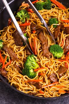 a pan filled with beef, broccoli and carrots being stirred by tongs