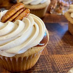 cupcakes with frosting and pecans on top sitting on a wooden table