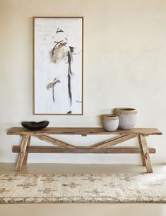 a wooden bench sitting in front of a painting on the wall next to a rug