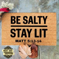 a mat with the words be salty stay lit next to autumn leaves