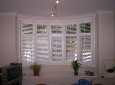 a living room with white shuttered windows and a tv in the corner next to it