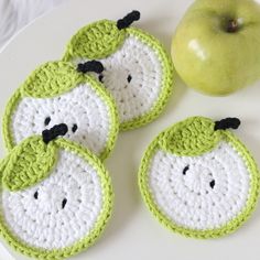 three crocheted apples are sitting on a white plate next to an green apple