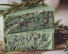 two bars of soap sitting on top of each other next to rosemary sprigs