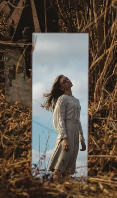 a woman standing in front of a mirror with her hair blowing in the wind and looking up into the sky