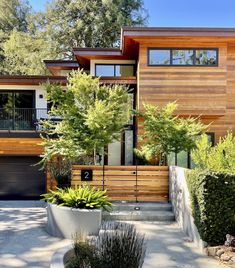 a modern house with wood siding and plants in the front yard