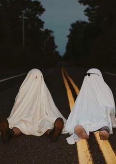 two people in white cloths sitting on the side of a road next to each other