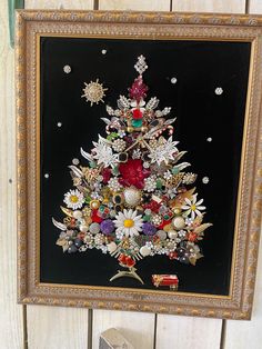 a christmas tree made out of flowers in a gold frame on a white wooden wall