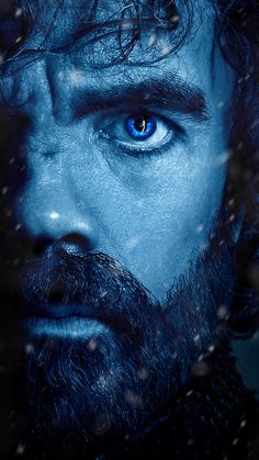 a man with blue eyes stares into the distance in front of snow falling on his face