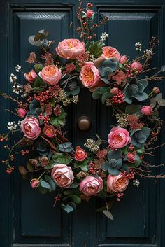 a wreath with pink flowers and greenery is hanging on a blue front door,