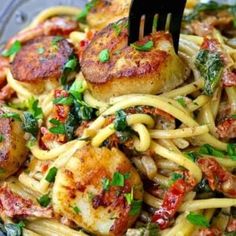 pasta with scallops and spinach in a glass bowl being held by a fork