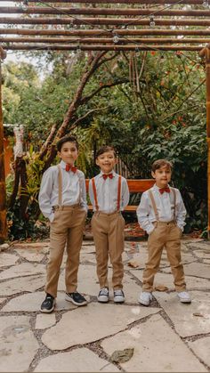 three young boys wearing suspenders and bow ties standing in front of a pergolan