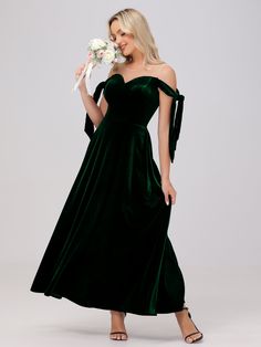 a woman in a green velvet dress holding a white flower and posing for the camera