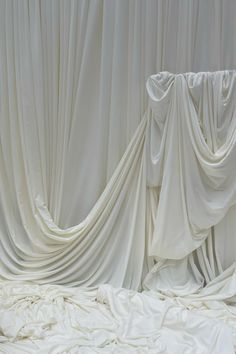 an unmade bed covered in white sheets and drapes