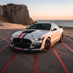 a white sports car parked in front of the ocean with red, white and blue stripes