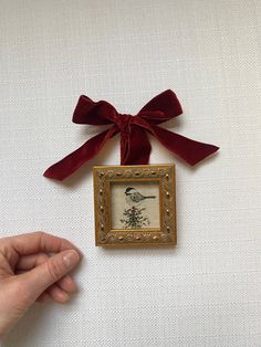 a hand holding a small framed painting with a red bow on it's head