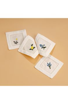 four embroidered napkins with flowers on them sitting on a tan surface, one folded and the other closed