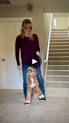 a woman standing next to a brown dog on top of a carpeted floor in front of stairs