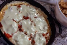 a close up of a pizza in a pan with cheese on top and chips next to it