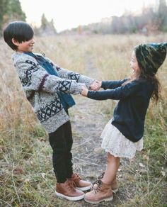 two young children holding hands and standing in tall grass with trees in the back ground