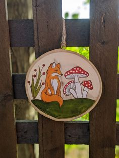 a hand painted wooden sign with a fox and mushrooms on it hanging from a fence