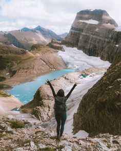 a woman standing on the side of a mountain with her arms up in the air