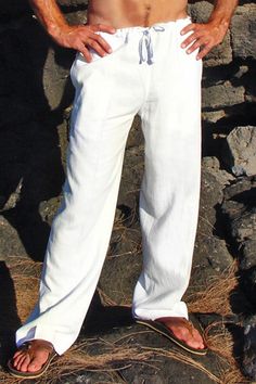 a shirtless man standing on top of a rock next to a black dog and wearing white pants