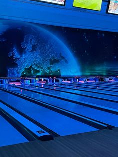 the bowling lanes are lined up against the blue wall and there is a large television screen behind them