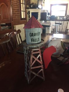 a wooden tower with a sign that says gravity falls on it's side in the middle of a dining room