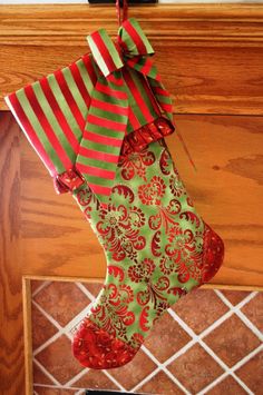 a christmas stocking hanging from a fireplace with red and green ribbons on it's side