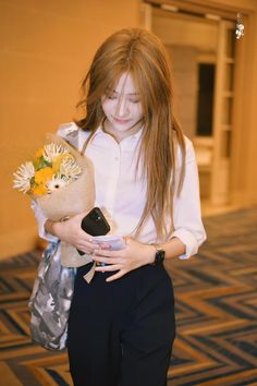 a girl with long hair is holding a bag and looking at her cell phone while wearing a white shirt