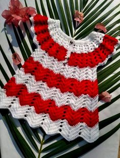 a red and white crocheted baby dress sitting on top of a palm leaf