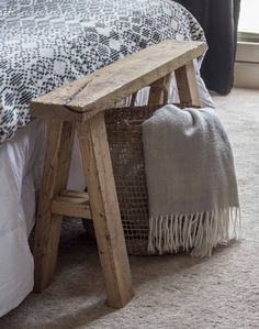 a wooden bench sitting on top of a bed next to a white pillow and blanket