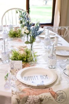 the table is set with white plates and flowers