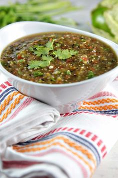 a white bowl filled with green salsa on top of a striped napkin next to lettuce