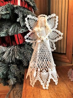 an angel made out of crochet sits on a table next to a christmas tree