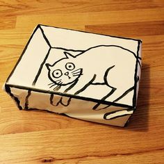 a white box with a drawing of a cat on it's side sitting on a wooden floor