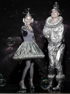 a man and woman dressed in silver standing next to each other with bubbles floating around them