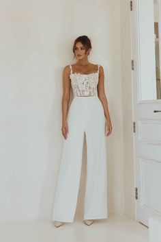 a woman standing in front of a white wall wearing a crop top and wide legged pants