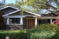 a house with trees and flowers in the front yard, behind a wooden picket fence