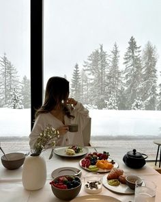 a woman sitting at a table with plates of food and drinks in front of her