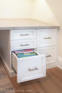 an open file cabinet in a room with hardwood flooring and white drawers on both sides