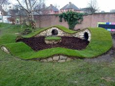 an outdoor area with green grass and rocks, including a small cave in the middle