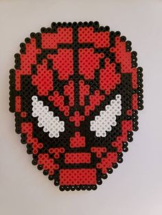 a red and black skull made out of perler beads on a white surface,